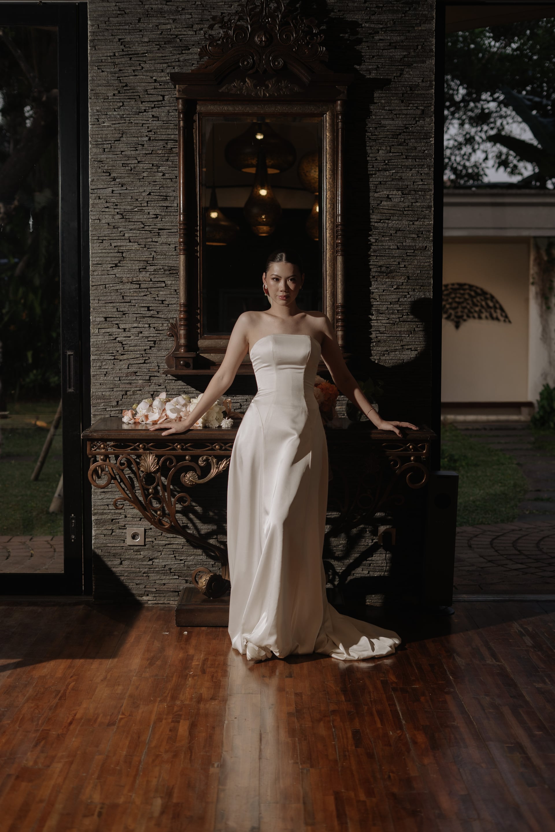 A bride in a strapless gown standing before a carved mirror.