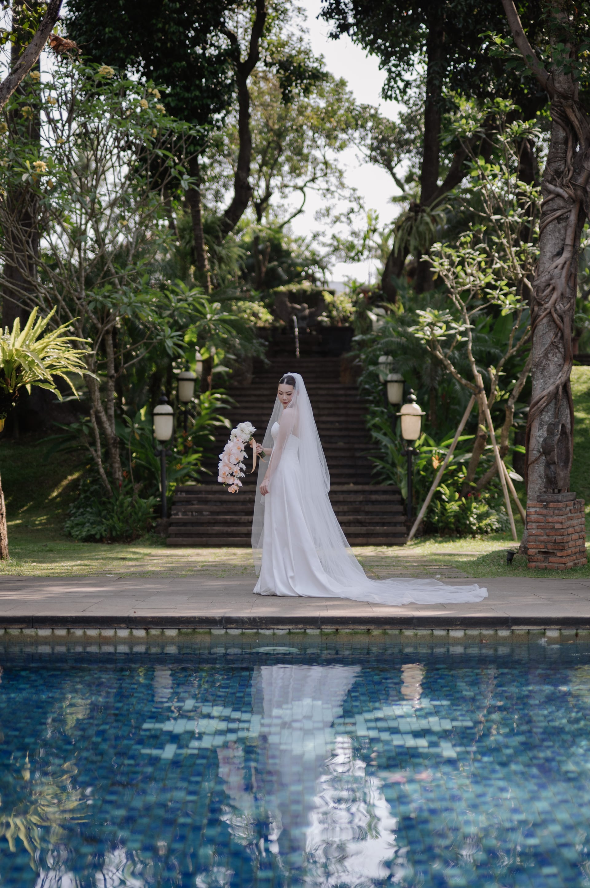 A bride beside the pool, holding a cascade of orchids.